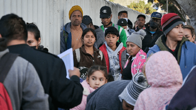 Image caption: Migrants wait in line while California border activists organize the group to enter the U.S. and seek asylum through the Chaparral entryway in Tijuana, Mexico on Dec. 22, 2022.