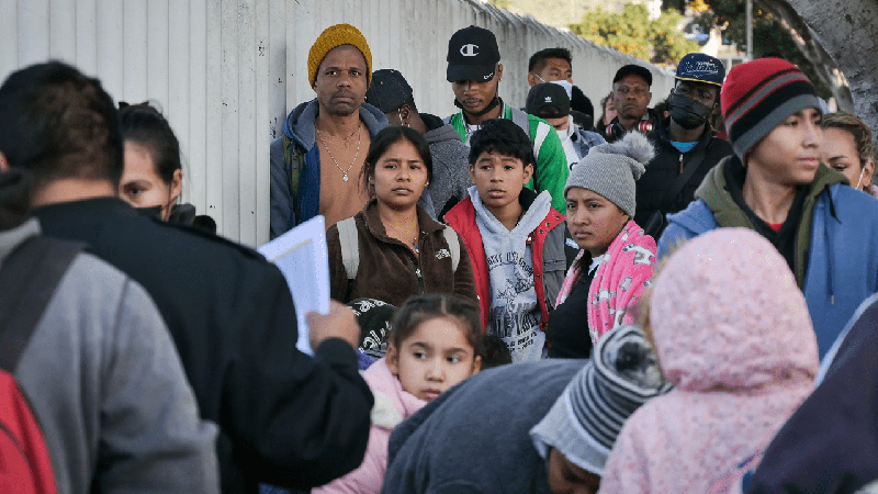 Migrants wait in line while California border activists organize the group to enter the U.S. and seek asylum through the Chaparral entryway in Tijuana, Mexico on Dec. 22, 2022.
