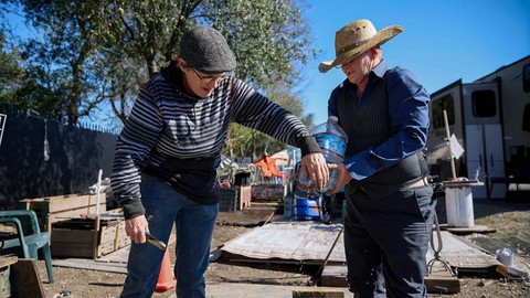 Image caption: Joyce and Sharon Jones poke holes in a water bottle to water their garden next to their trailer at Camp Resolution on Feb. 28, 2024. The camp has no running water, so residents must rely on bottled water for all their needs.