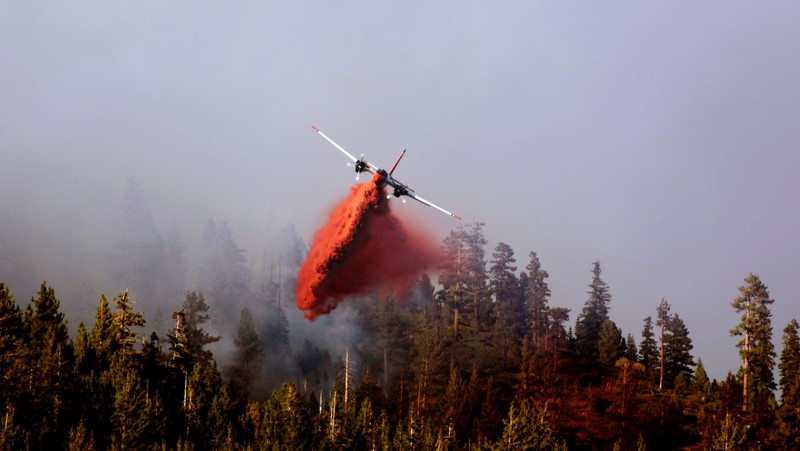 A CalFire tanker aircraft drops a plume of fire retardant on a forest.