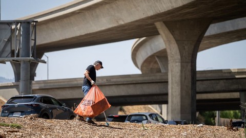 Image caption: Gov. Gavin Newsom walks through a homeless camp with a garbage bag.