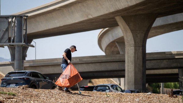 Gov. Gavin Newsom walks through a homeless camp with a garbage bag.