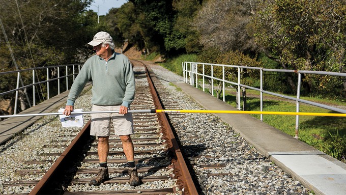 Image caption: Miles Reiter, an opponent of rail and a board member for Greenway, walks the railroad tracks with a pole to show the width of the corridor.