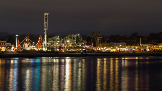 Image caption: Lights along the Santa Cruz Beach Boardwalk look pretty reflected in the Pacific Ocean, but the brightness wreaks havoc on the starry skies above.