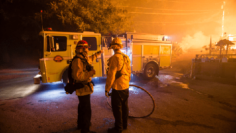 Image caption: Firefighters stand outside a burning home in Boulder Creek, CA, in August 2020.