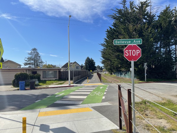 The intersection of the rail trail with Bellevue Avenue, looking east.
Note the yellow lane divider poles at the intersection, high viz crosswalk and signage.