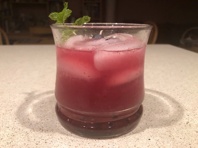 Pink-purple cocktail in glass with mint sprig