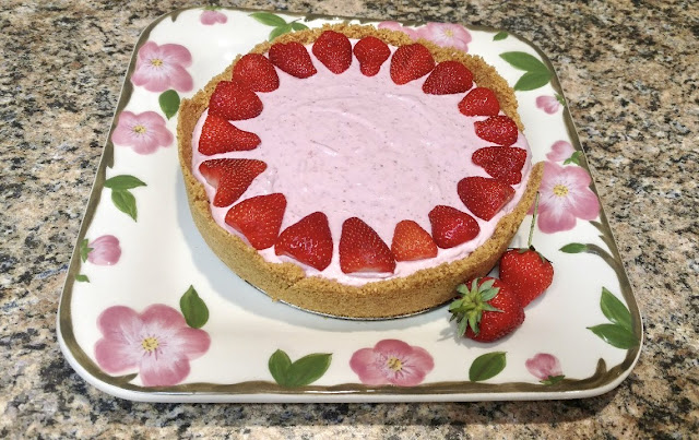 Pink strawberry cheesecake on white plate with pink flowers and green leaves