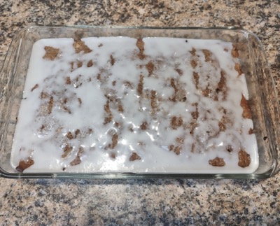 Baked  in a glass pan, a coffee cake with a sugary white glaze