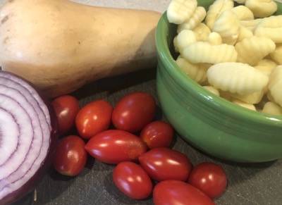 Bowl of gnocchi with red onion half, several small tomatoes and a butternut squash