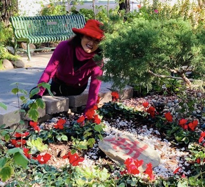 Woman in red hat and magenta sweater in  a garden