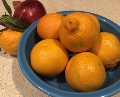 6 mandarin oranges in a blue bowl, with a pomegranate and another mandarin alongside