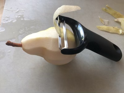 A Bartlett pear with a peeler pulling off a slice of skin