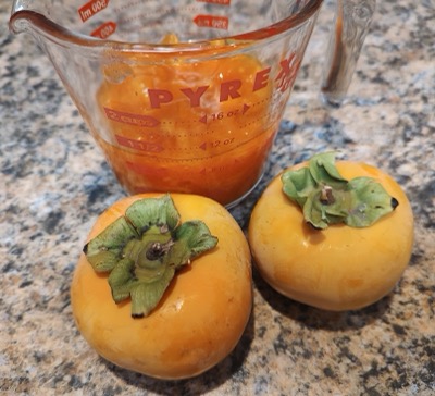 Two persimmons and a measuring cup of pulp