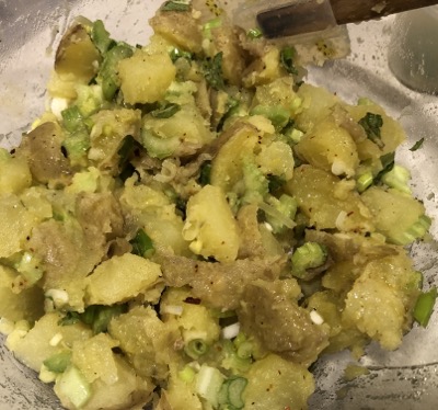 Clear bowl with potato salad being mixed