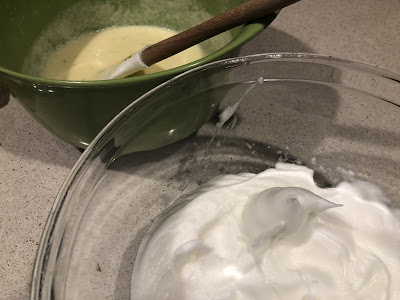 Egg whites in bowl in front of a green bowl with yellow batter