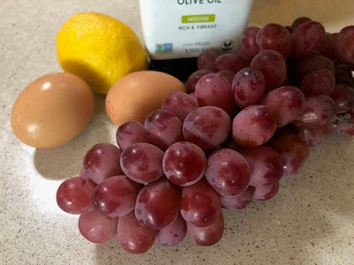 Olive oil, red grapes, a lemon and two brown eggs