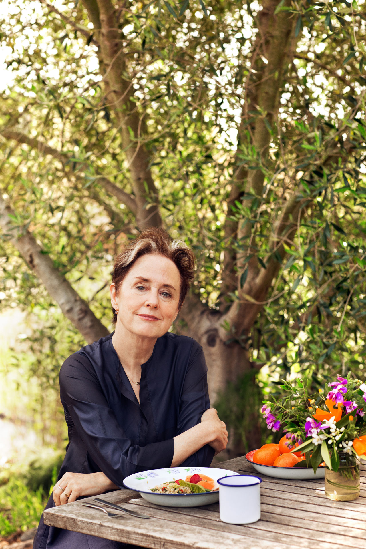 Alice Waters outdoors in front of a table with food and flowers
