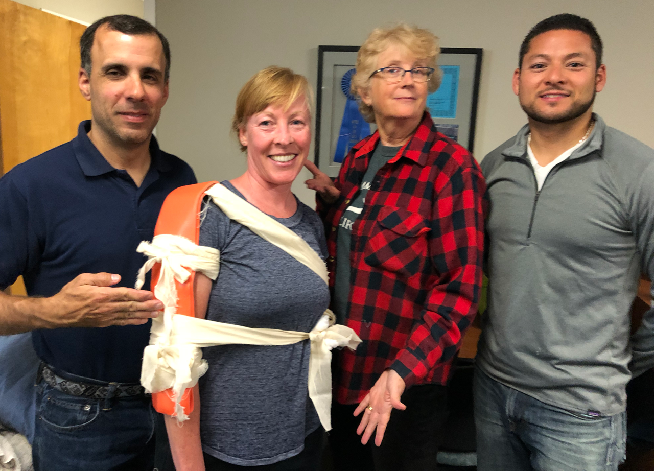 Man applies a bandage to a woman’s arm in a room full of other volunteers